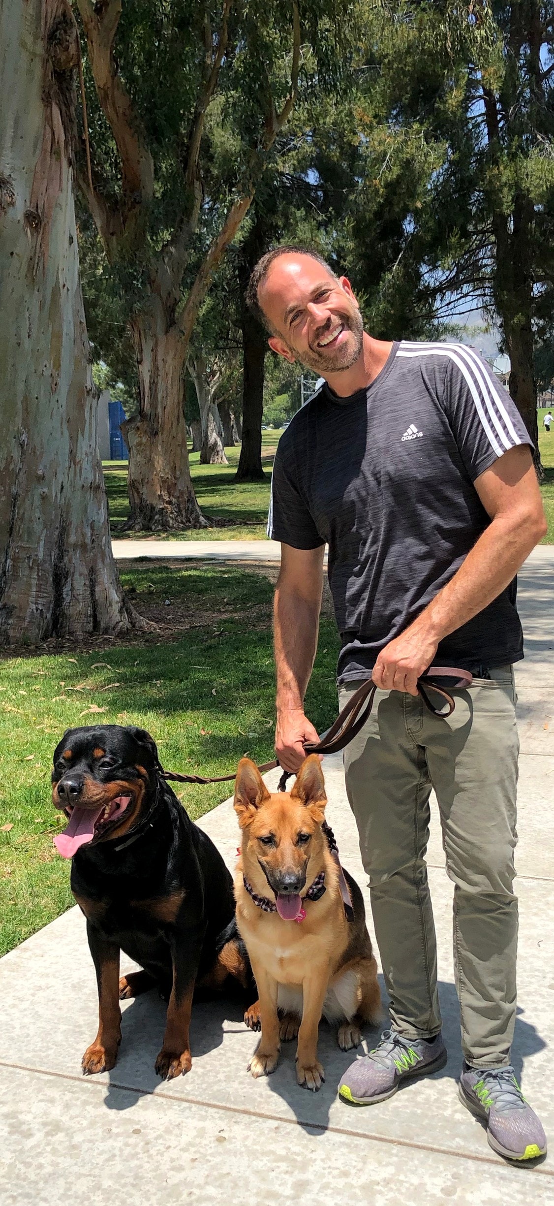 Brett Endes with a Rottweiler and a German Shepherd sitting on a loose leash at a park